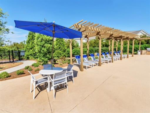 A row of lounge chairs and a picnic table on the pool sundeck near trees and bushes