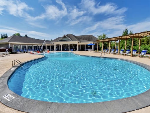 Sparkling pool with fountains, and lounge chairs under a wooden pergola near a clubhouse