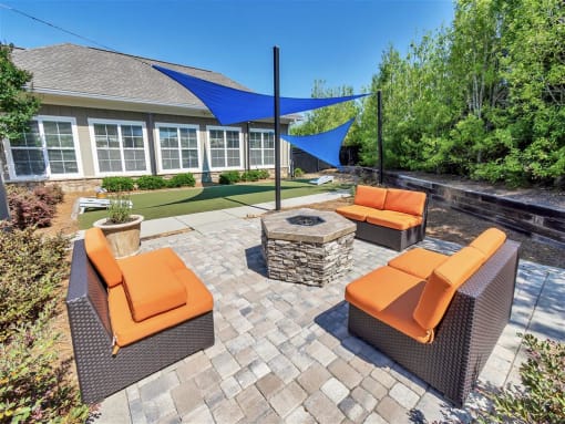 Outdoor cushioned chairs surrounding a fire pit on a cobblestone patio with a shaded grassy area