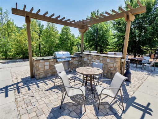 Grilling station with small wooden pergola, outdoor bar, and tables with chairs near trees