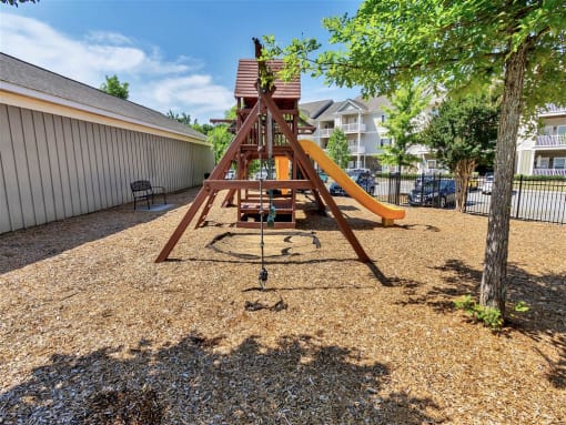 Rope hanging from the playground on a floor of wood chips  near a bench, street parking, and trees