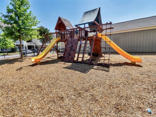 Gated playground with wood chips on the ground near trees and apartment complexes