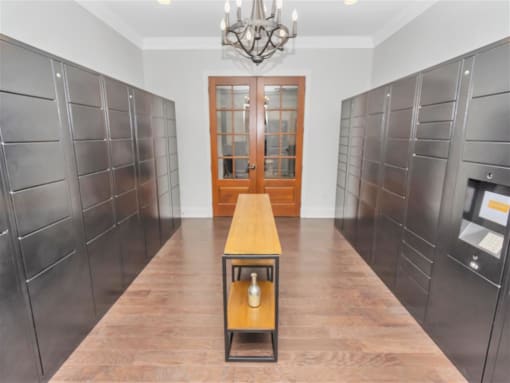 Mail room for package pick up with hanging chandelier, slender table in the middle and double doors