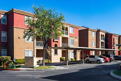 A row of apartment buildings with cars parked in front.