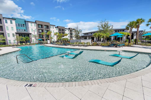 a resort style pool with chaise lounge chairs and umbrellas in front of an apartment
