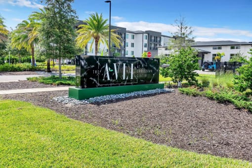 a sign in the middle of a grassy area with buildings in the background
