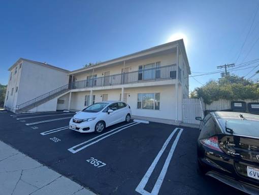 A white car is parked in a parking lot in front of a building.
