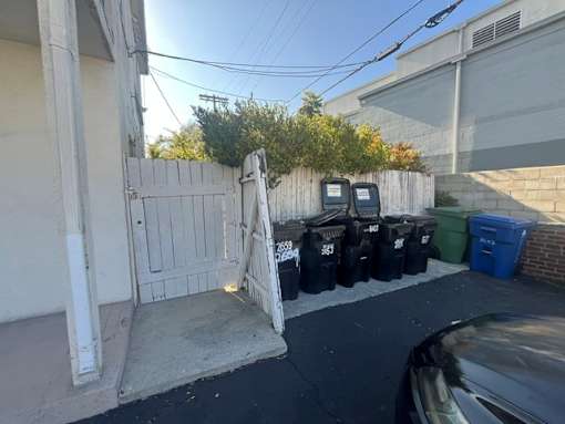 A white gate is open to a driveway with a black car parked in front.