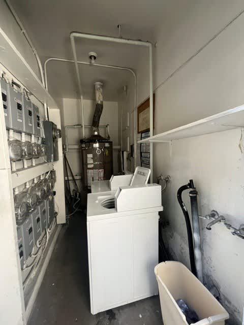 A white washing machine is in a small room with a lot of pipes.