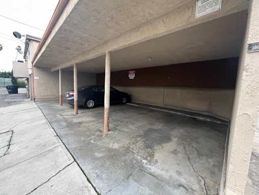 A car is parked in a garage under a no parking sign.
