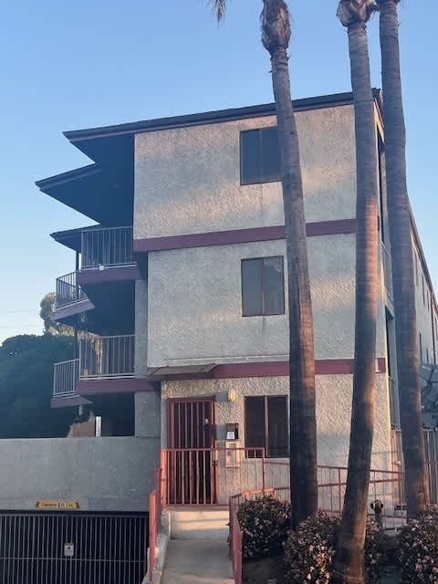 A two-story building with a balcony and palm trees in front.