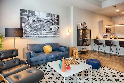A living room with a black and white photo on the wall, a blue couch, a black leather chair, a white coffee table, and a black and white rug.