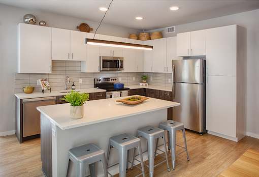 A kitchen with white cabinets and a white island with three stools.