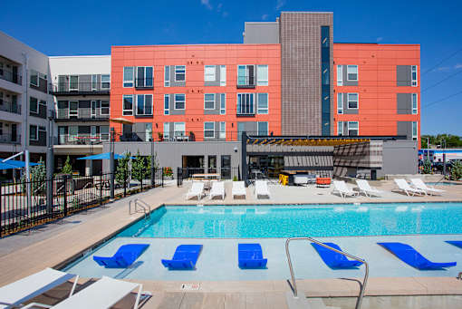 A pool with blue loungers and chairs in front of a red building.