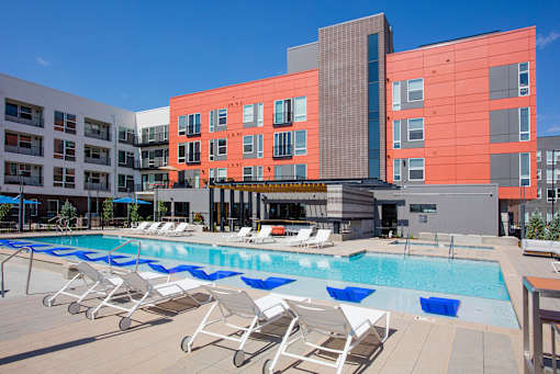 A pool with lounge chairs in front of a red building.