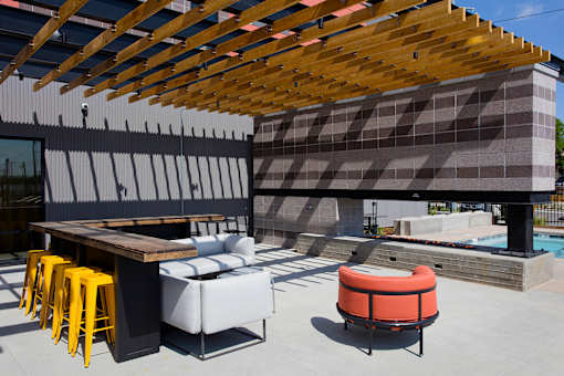 A modern outdoor seating area with a wooden roof and a pool in the background.