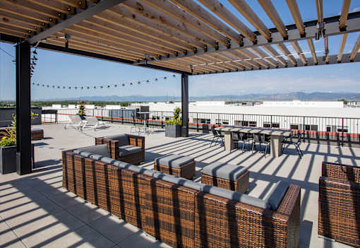 A patio with a wooden pergola and wicker furniture.