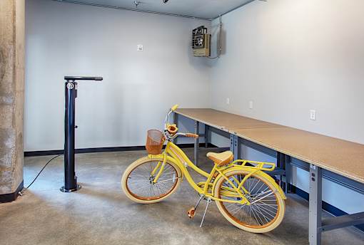 A yellow bicycle with a brown seat is parked in a room with a blue pole and a white wall.