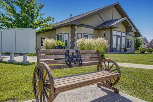 A wooden bench with a wagon wheel design is in front of a house.