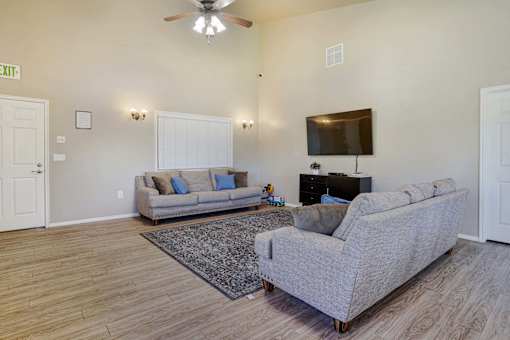 A living room with a grey couch, a rug, a ceiling fan, and a flat screen TV mounted on the wall.