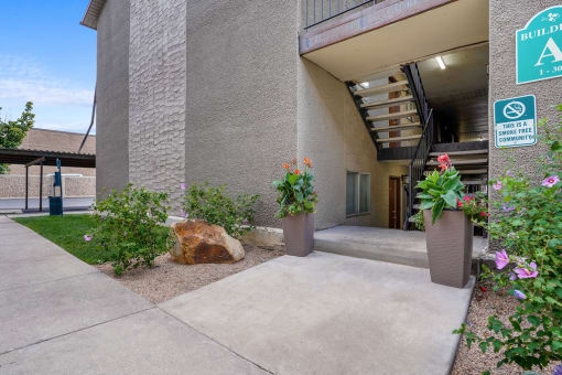 a sidewalk in front of a building with plants and a rock