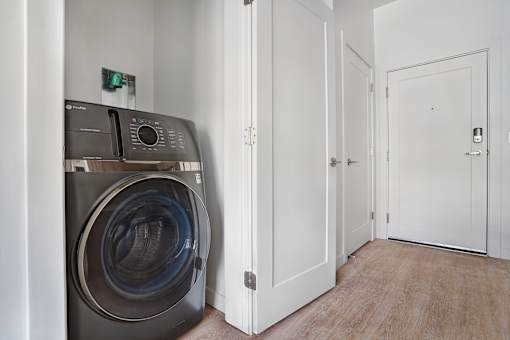 A washing machine is in a small room with a door on the right.