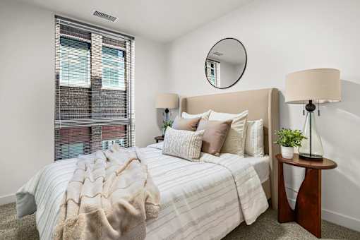 A bedroom with a bed, a lamp, and a mirror on the wall.