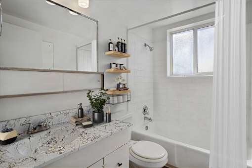 A white bathroom with a marble counter top and a white toilet.