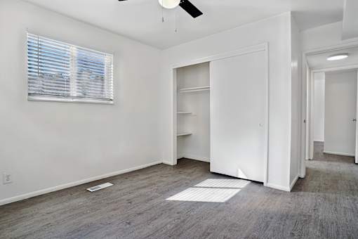 A room with a white door, a window with blinds, and a ceiling fan.