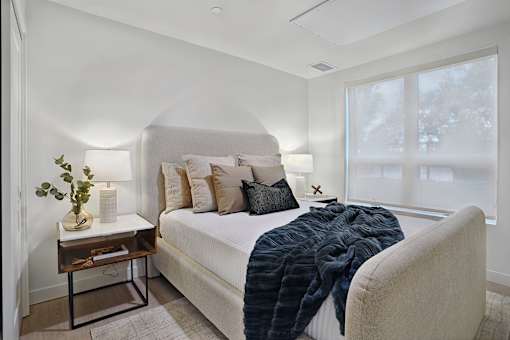 A bedroom with a bed, a chair, and a table with a plant on it.