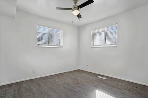 A room with a ceiling fan and two windows.