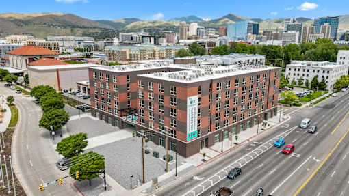 A large red brick building with a green sign on the side is in the middle of a busy street.