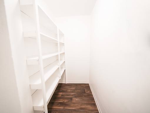 A long white shelving unit with multiple shelves is in a room with wooden floors.