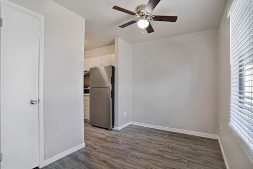A room with a ceiling fan and a refrigerator in the corner.