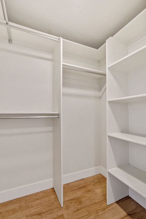 a walk in closet with white shelves and a wood floor