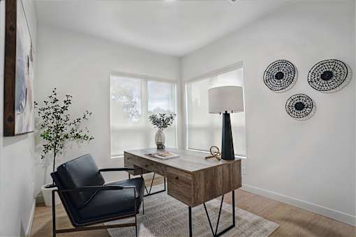 A black chair sits in front of a desk with a lamp on it.