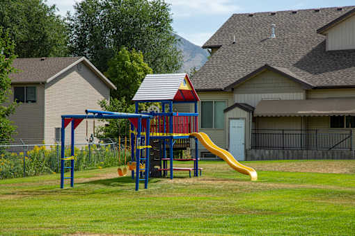 a playground with a yellow slide in a park with houses in the background