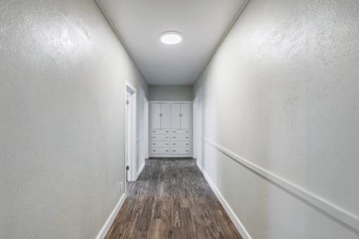 an empty hallway with white walls and wood floors and a closet