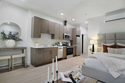 A modern bedroom with a large bed and a kitchen area in the background.