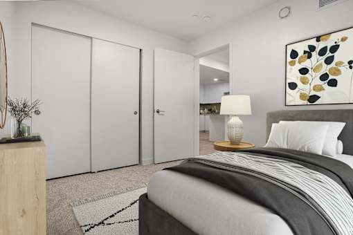 A bedroom with a bed, a nightstand with a lamp, and a painting on the wall.