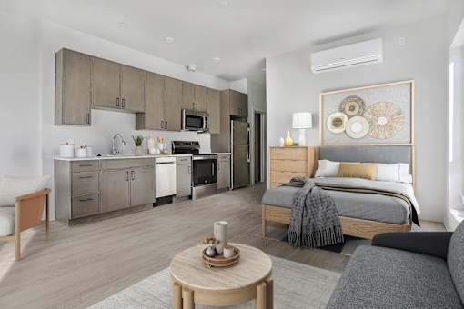 A modern bedroom with a large bed and a kitchen area in the background.