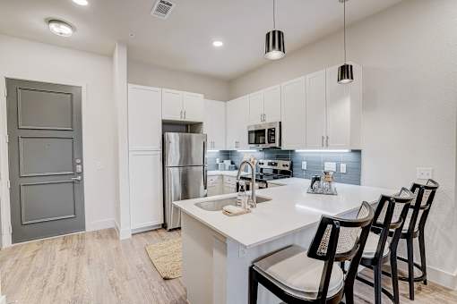 Modern kitchen with island seating and white cabinetry at The Mill Old Town Apartments, Lewisville, TX 75057
