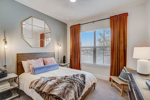 Bedroom with wooden bed frame and large mirror at The Mill Old Town Apartments, Lewisville, TX