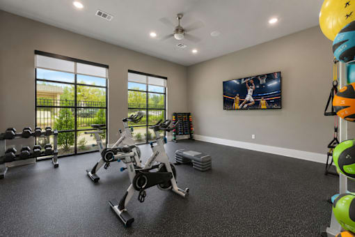 Fitness center with exercise equipment, large windows, televisions, and open workout space at Auberge of Tyler.