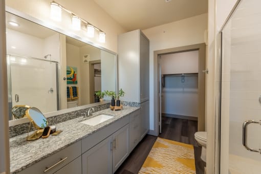 a bathroom with gray cabinets and a yellow rug at One Preston Station, Celina, TX