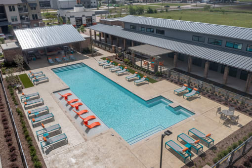 an aerial view of a swimming pool with chaise lounge chairs and a building in the background at One Preston Station, Celina