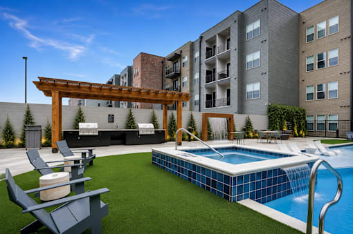 A pool with a slide and a pergola in the foreground with apartment buildings in the background.