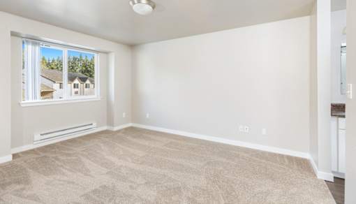 A room with a carpeted floor and a window showing a view of houses.