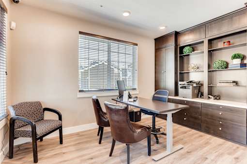 A room with a desk, chairs, and a cabinet with shelves.