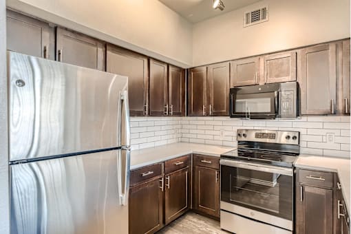 A kitchen with a stainless steel refrigerator, microwave, oven, and cabinets with quartz countertops.
